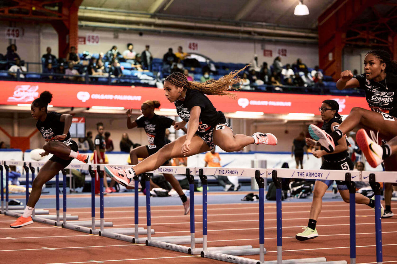 Grupo de atletas saltando vallas en una pista de atletismo como parte de los «Juegos Femeninos de Colgate».
