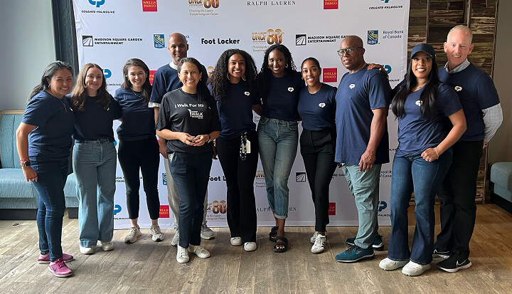 Un grupo de personas en el evento del «United Negro College Fund», posando para una foto frente a una pared con los logotipos de los patrocinadores. 